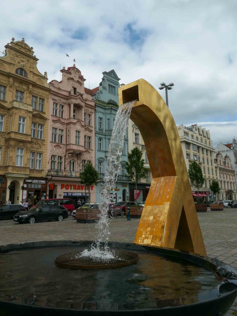 Goldene Skulptur mit Wasser vor bunter Häuserfassade am Platz der Republik in Pilsen. Foto: Lisa Freudlsperger