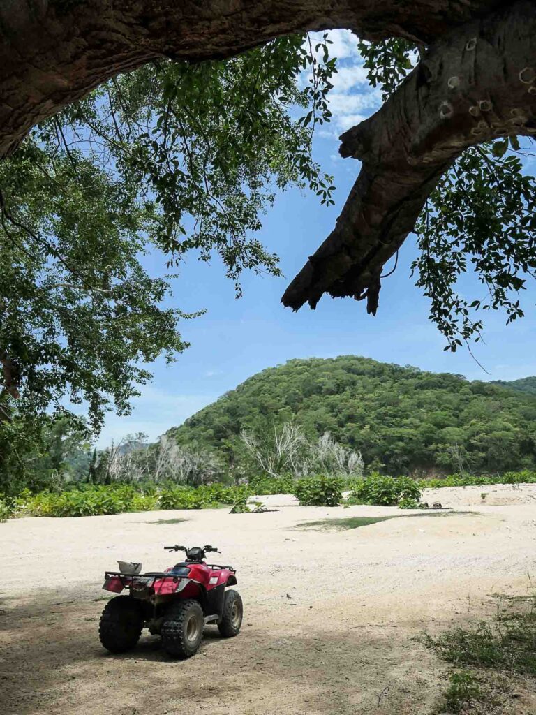 Quad steht vor trockenem Flussbett und bewaldeten Hügeln. Foto: Lisa Freudlsperger