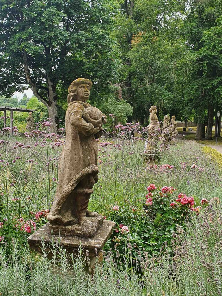 Steinerne Statuen zwischen Blumen und langen Gräsern