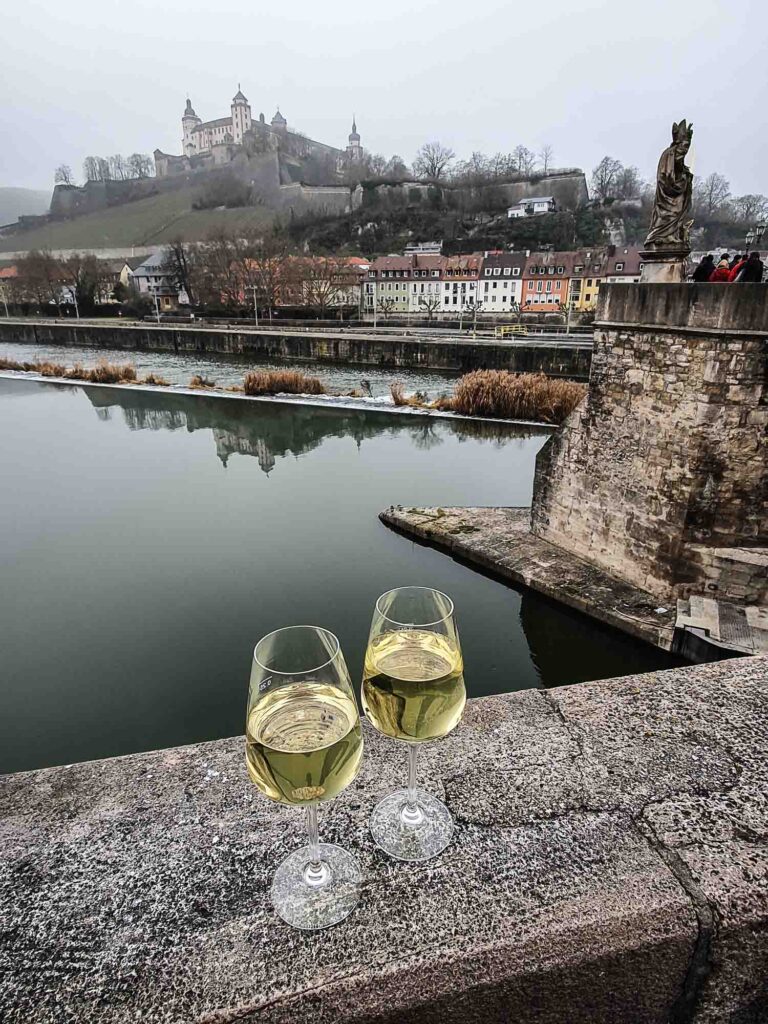 Zwei Weingläser auf Steinbrücke mit Fluss und Burg im Hintergrund Foto: Lisa Freudlsperger