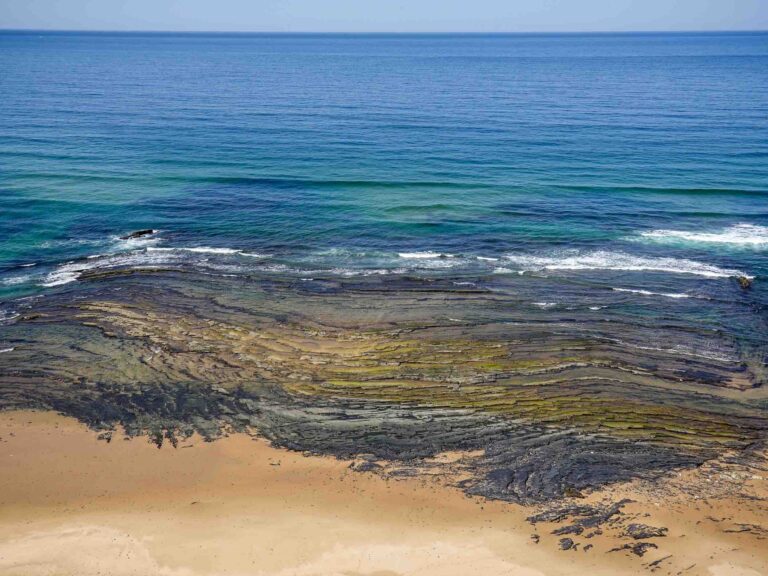 Blick auf Felsstrukturen zwischen Sandstrand und offenem Meer Foto: Lisa Freudlsperger