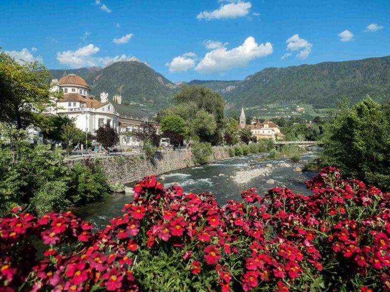 Blick auf Fluss und Berge, zur Linken das Meraner Kurhaus, im Vordergrund rote Blumen. Foto: Lisa Freudlsperger