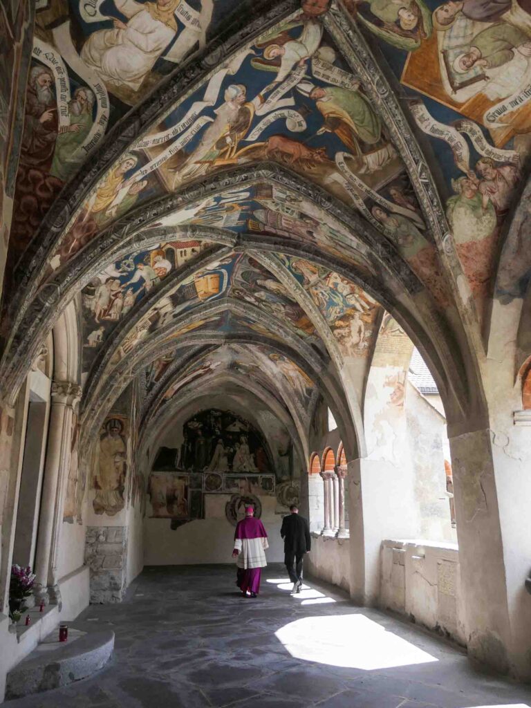 Zwei Geistliche spazieren durch Kreuzgang mit aufwendig bemalter Decke in Brixen. Foto: Lisa Freudlsperger