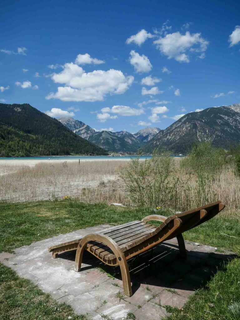Ein Liegestuhl aus Holz steht nahe des Bergseeufers. Foto: Lisa Freudlsperger